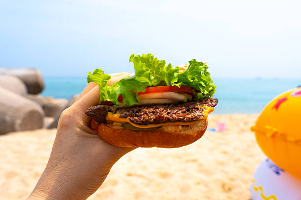 istock Woman holding burger in a hand against beach background 2229320974