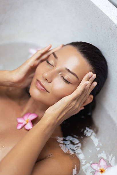 istock Asian Woman Gently Touching Face While Relaxing in Spa Bath With Flowers 2229322964