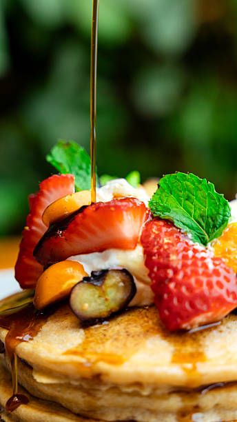 Delicious pancakes with syrup, berries, and cream being prepared