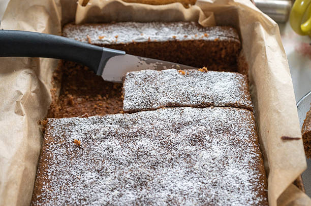 High-angle view of a knife cutting a carrot sheet cake dusted with powdered sugar.