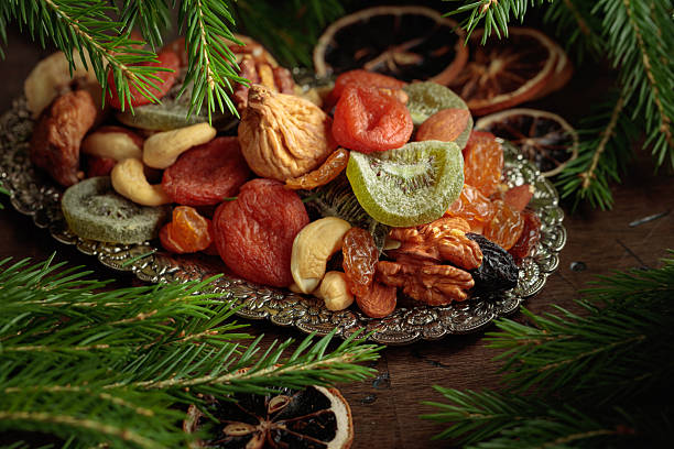 Assorted dried fruits and nuts on a silver tray. Vegetarian dessert and Christmas tree branches on an old wooden table.