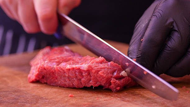 istock Skilled butcher cutting fresh beef in store with sharp knife and professional technique 2229345639