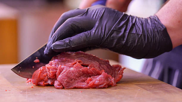 Skilled butcher cutting fresh beef in store with sharp knife and professional technique.