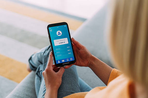 istock Young woman using mobile app on smart phone for checking her finances while sitting on the sofa at home. 2229347331