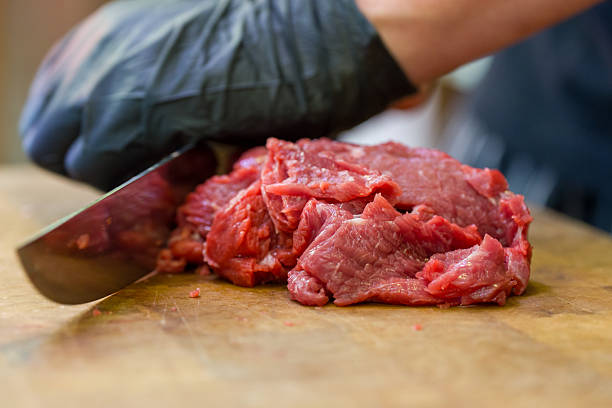 Man in black coat preparing meat cuts behind counter inside local meat shop.