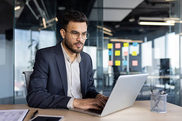 istock Focused businessman working on laptop in a modern office setting, typing at his desk. 2229349297