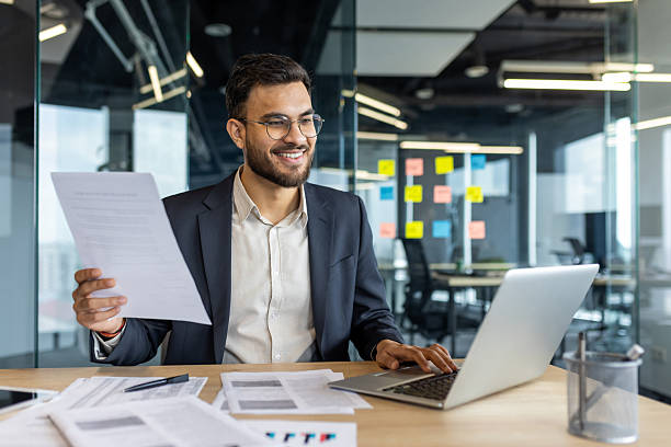 istock Happy businessman working on laptop and reviewing documents in modern office setting. 2229349337