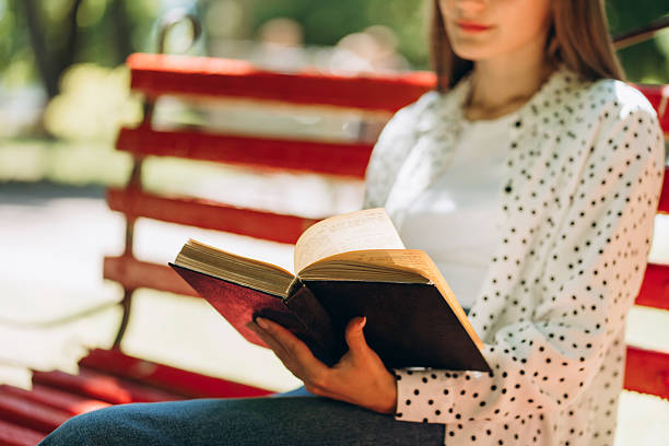 istock Young woman reading a book on park bench in summer 2229349484