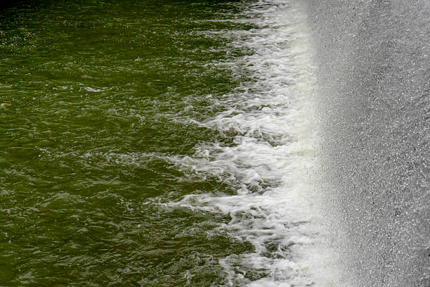 Water rushes down the dam wall, creating a dynamic contrast of textures between the falling water and foamy ripples below. A powerful and natural outdoor water scene.