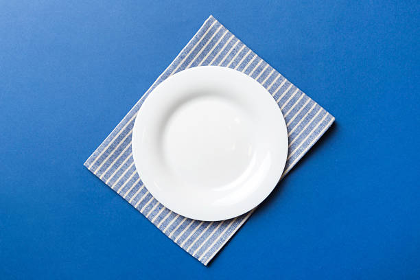 istock Top view on colored background empty round white plate on tablecloth for food. Empty dish on napkin with space for your design 2229351267