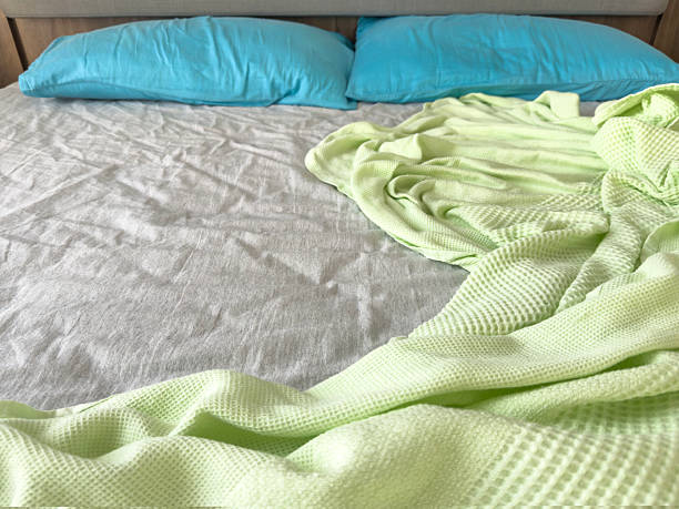 istock Unmade Bed with Blue Pillows and Light Green Blanket in morning 2229354891