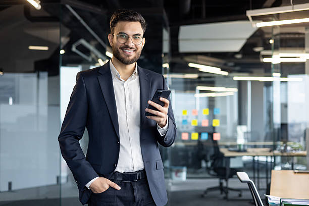 istock A businessman smiling in a suit holding a phone inside a modern office. 2229357077