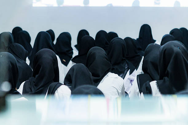 Gathering together, many Indonesian female students wearing black hijabs attentively listen to a presentation projected on a white wall during an engaging conference
