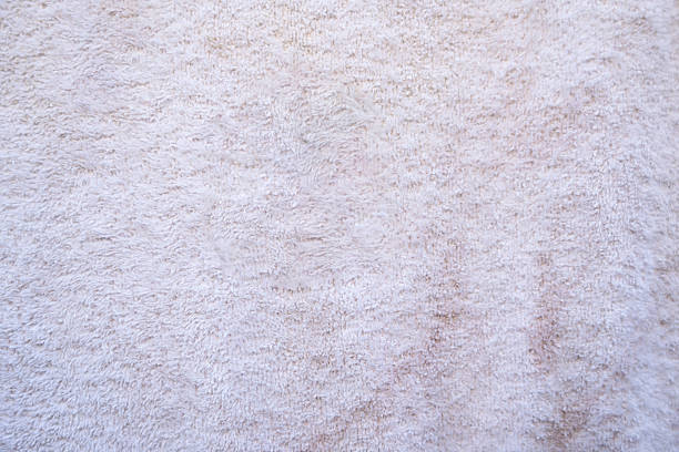 This image presents a detailed close-up view of a white terry cloth towel. The texture is soft and fluffy, with visible looped fibers creating a plush appearance.  There are subtle variations in tone, suggesting slight shadowing and perhaps minor discoloration in places. The overall impression is one of softness and absorbency, ideal for use as a background or texture in various design projects.