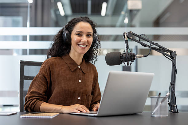 istock A woman happily prepares for her podcast, using a microphone and laptop in a modern studio setting. 2229365561