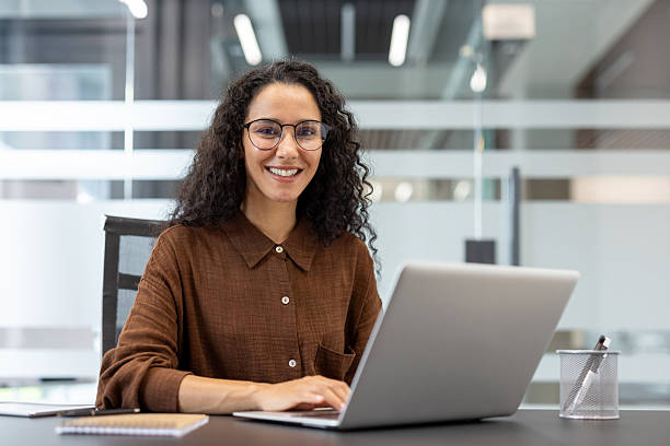 istock A cheerful woman with glasses using a laptop at her office desk. 2229365582