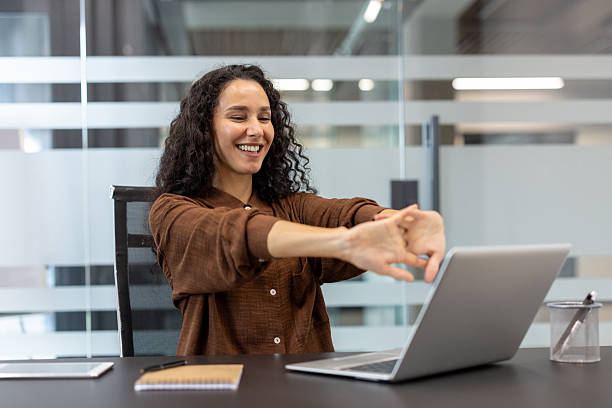 Happy woman stretching and smiling at her desk during a work break.