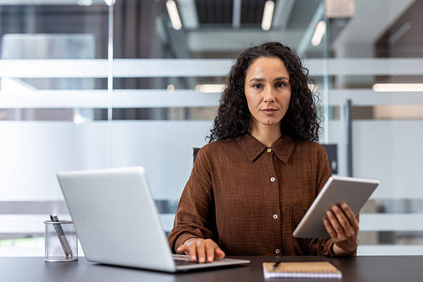 istock A determined businesswoman in a modern office setting, working on a laptop and a tablet. 2229365625