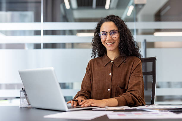 istock A confident woman smiles while working on her laptop in a bright office setting. 2229365655