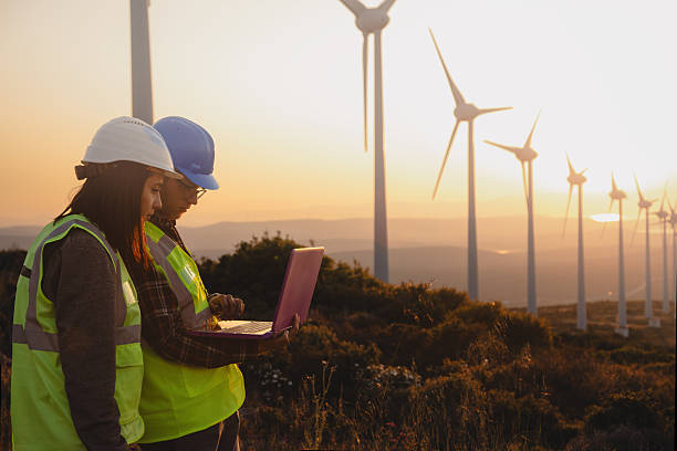 istock Engineers with Safety Helmets and Vests Using Laptop at Wind Farm During Sunset, Highlighting Renewable Energy, Sustainability, and Green Technology Innovation 2229378337