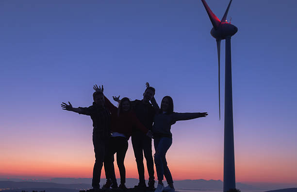 istock Group of Friends Posing with Open Arms at Wind Farm During Blue Hour, Emphasizing Friendship, Joy, and Sustainability 2229378423