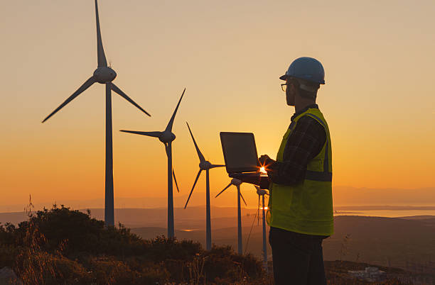 istock Male Engineer Using Laptop for AI-Assisted Wind Turbine Inspection at Sunset 2229378427