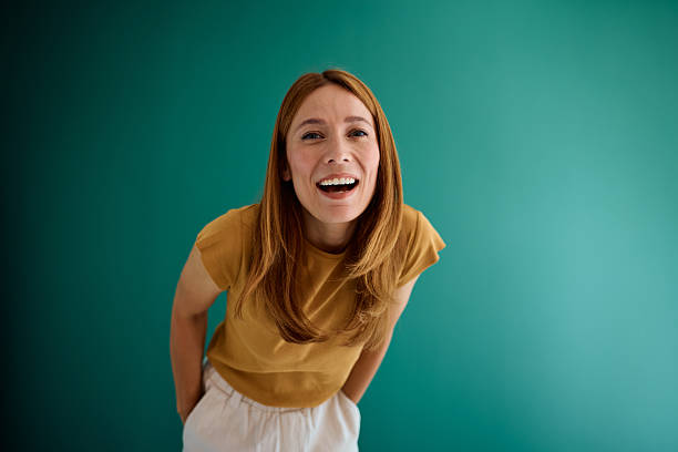 istock Woman laughing with hands in pockets on teal background 2229380458