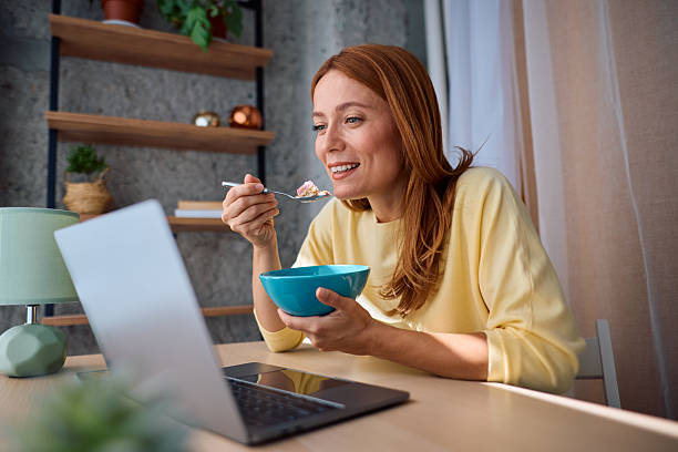 istock Smiling woman eating breakfast and looking at laptop 2229380711
