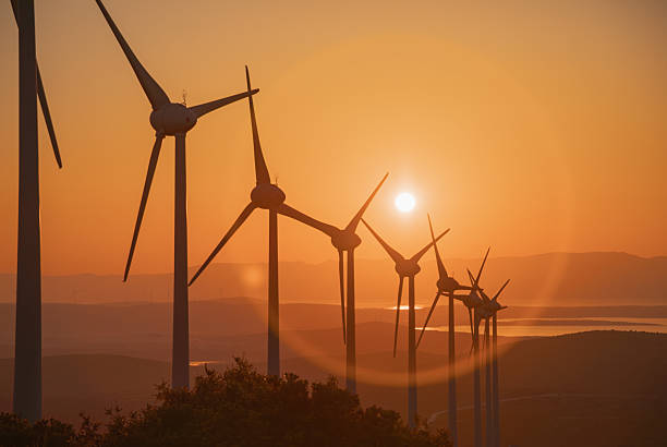 A striking silhouette of wind turbines under a warm, orange sunset sky. The image captures the renewable energy landscape at dusk, signifying clean energy, environmental innovation, and sustainable development in a serene, open-air setting.