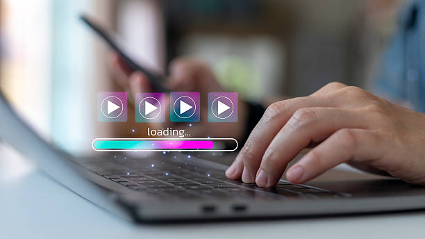 istock Person using laptop and smartphone with video streaming icons and loading progress bar, concept of online media, entertainment, and digital content technology. 2229387779