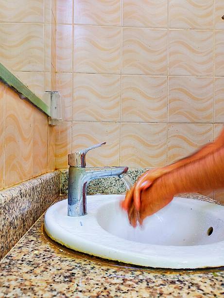 A photo of someone washing their hands at a sink with running water in a bathroom or kitchen.