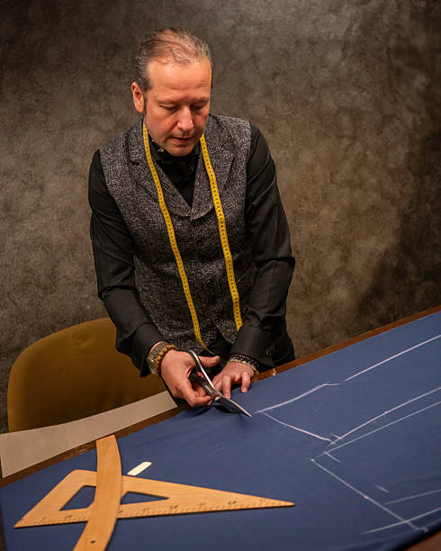 male fashion designer is cutting fabric in his studio miters are on fabric on table vertical small business still stock photo