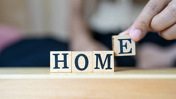 Wooden blocks spelling home, with hand adjusting letter E, creating warm and inviting atmosphere. This captures essence of comfort and belonging