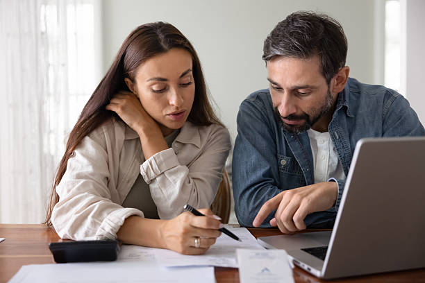 istock Couple review financial documents together seated at table with laptop 2229397986