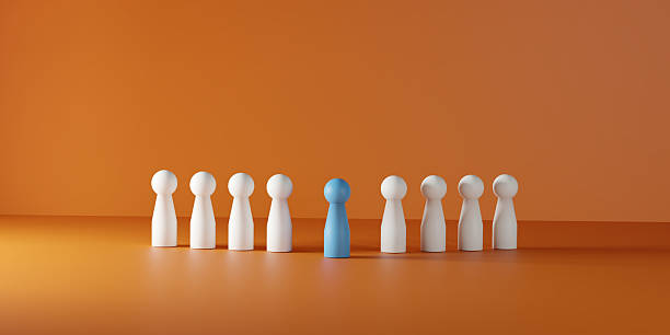 istock Individuality, leadership, being different, and standing out in a team or group. A single blue doll prominently positioned among a line of white dolls on a vibrant orange background. 2229402588