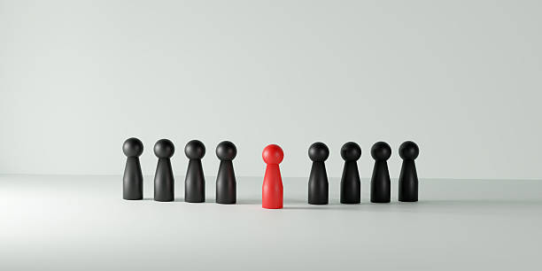 istock Individuality, leadership, being different, and standing out in a team or group. A single red doll prominently positioned among a line of black dolls on a vibrant white background. 2229402598