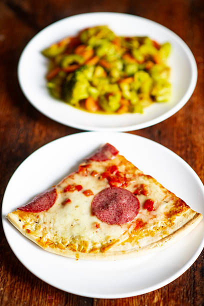 Pepperoni pizza slice with cheese and vegetables on white plates.