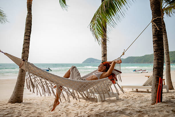istock Woman relaxing in a hammock between palm trees on a tropical beach, enjoying a peaceful day by the ocean with mountains in the distance 2229409849