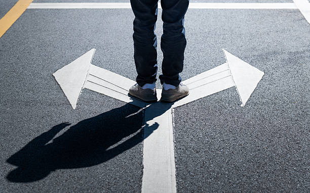 istock Man standing on road with two direction arrow and get to decision which way to go 2229421510