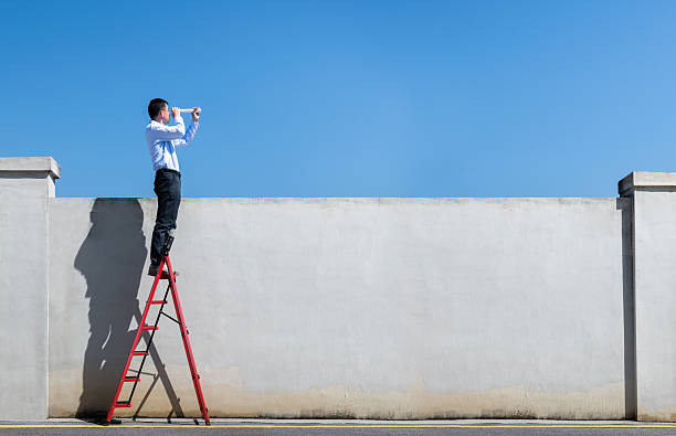 istock Businessman standing on ladder and watching through rolled up paper 2229421524