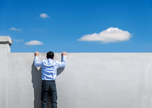istock Young businessman climbing over a concrete wall with blue sky 2229421530