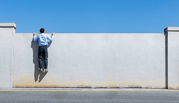 Young businessman climbing over a concrete wall with blue sky
