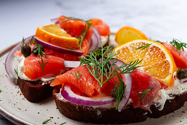 sandwich with freshly smoked salmon, on black bread, with cottage cheese, with herbs and red onions, capers and pieces of citrus fruits, on a marble countertop, breakfast, no people,