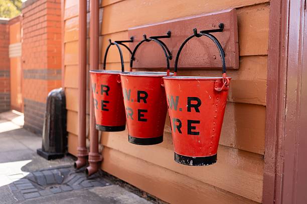 3 Vintage red fire buckets hanging on a wooden wall for emergency use.