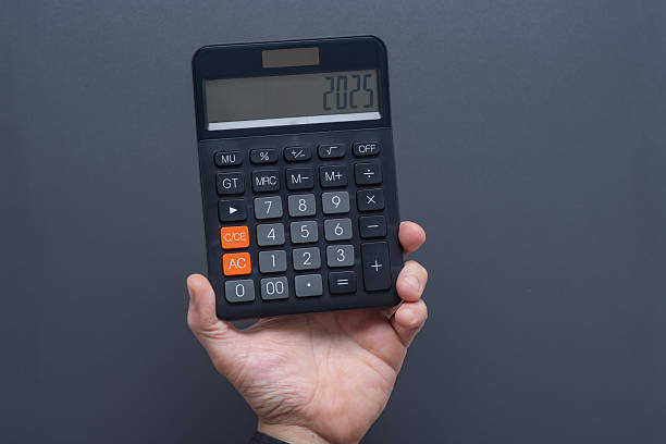 istock Man hand holding black digital calculator displaying 2025 on LCD screen against gray background. Business finance and annual planning concept for new year calculations and budgeting. 2229429155
