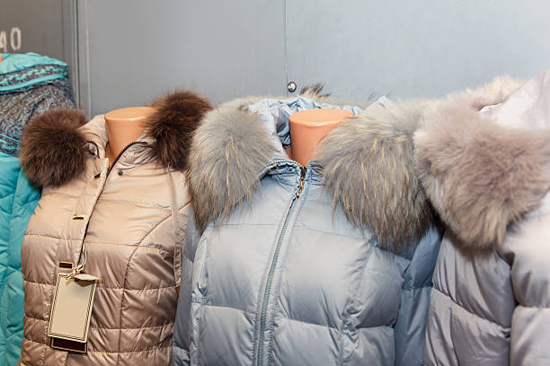 Row of warm winter jackets with fur collars on mannequins, in various colors, against an indoor backdrop. Concept of outerwear fashion