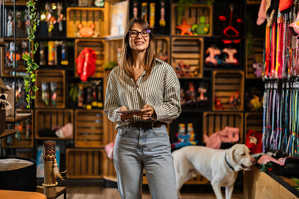 istock Female employee using a digital tablet while working in a pet shop, with a dog walking beside her. 2229436651