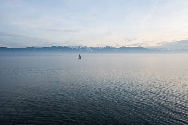 Peaceful Lake Constance landscape with misty haze over water and mountain silhouettes on horizon. Soft morning or evening light creating dreamy atmosphere in this Alpine region tourist destination.