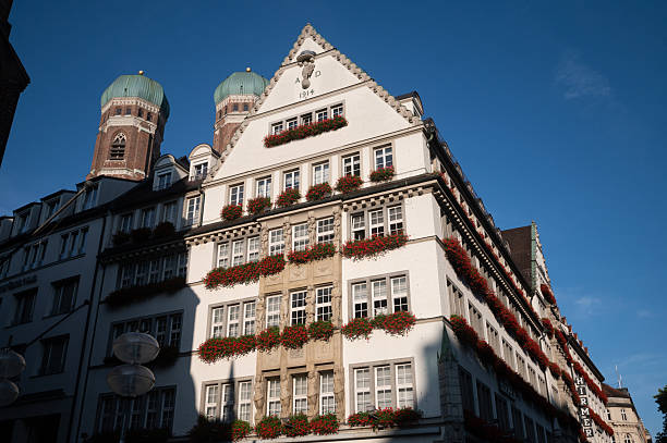 Historic building in Munich with characteristic Bavarian architecture, painted in light colors with dark red roof. Multi-story building with regular window arrangement and decorative facade elements.