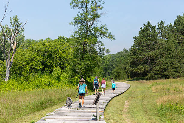 Rear view of a father and two kids walking down a wooden boardwalk at Crow Wing State Park in Minnesota, USA, on a summer day.